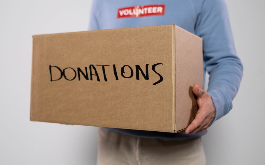 Man wearing a shirt with a 'volunteer' sticker holds a cardboard box labelled 'donations'